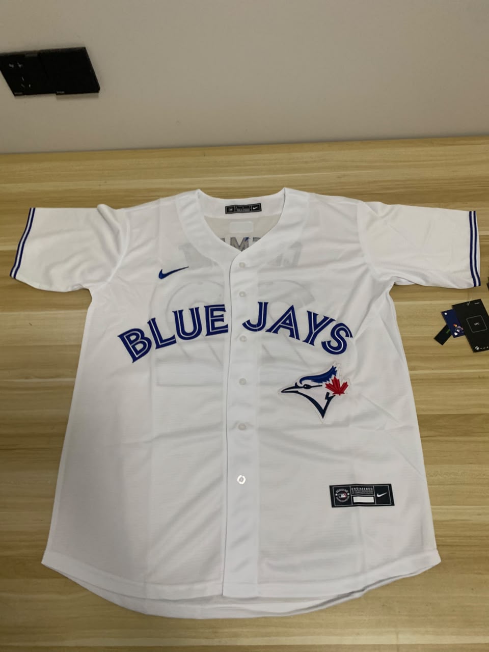 White baseball jersey with 'Blue Jays' logo on a wooden surface
